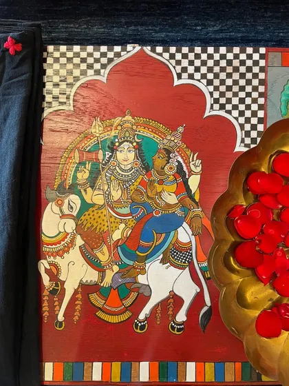 A close-up of the central panel depicting Shiva and Parvati, hand-painted in the Kalamkari style. The rich red background and intricate details showcase the fusion of devotional art with furniture restoration.