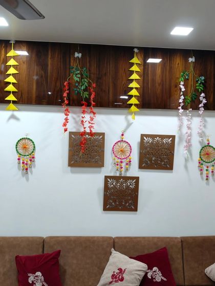 A simple yet elegant wall decoration for a home celebration. This setup features dream catchers, hanging floral vines, and paper craft against a dark wood-paneled wall.