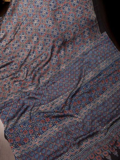 A close-up of a black saree with intricate blue and red block prints. The detailed patterns create a beautiful tapestry effect.