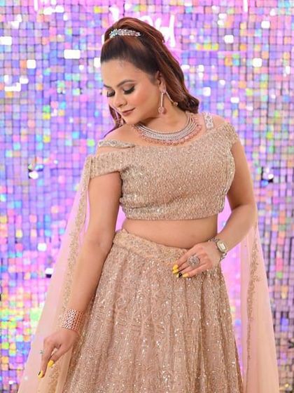 A client posing against a glittering backdrop in the champagne gold lehenga, looking ready for a party.