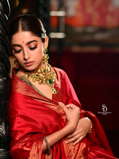 A soft and contemplative portrait of Ishaa Saha. Her eyes are closed, and the lighting gently falls on her face, highlighting the rich gold and emerald necklace.