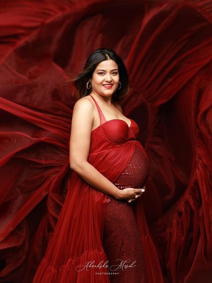 A radiant smile from the mother-to-be, wrapped in a dramatic red gown with a sequined bodice and flowing tulle.