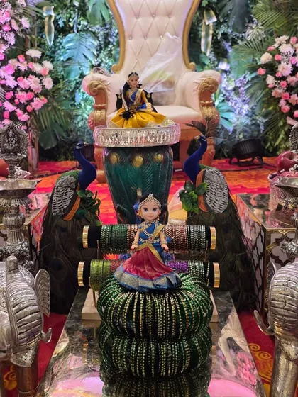 A close-up of the decor for a puberty ceremony, featuring dolls dressed in half-sarees and stacks of bangles.