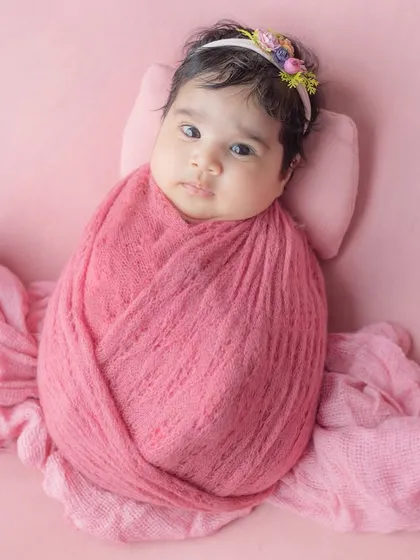 A classic swaddled pose on a soft pink backdrop, showing off the baby's beautiful eyes.
