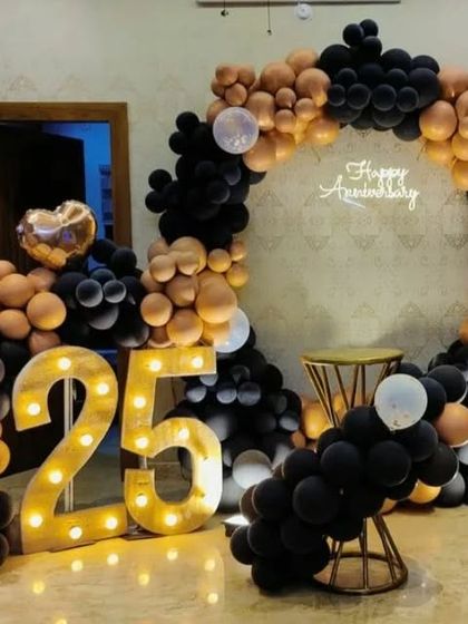 A stylish 25th anniversary setup with a circular organic balloon arch in black and rose gold, paired with illuminated marquee numbers. This design is modern, elegant, and highly photogenic.