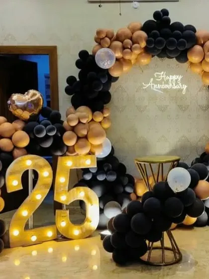 A modern and chic 25th anniversary setup in black and muted gold. The organic balloon arch and light-up numbers create a sophisticated and trendy vibe.