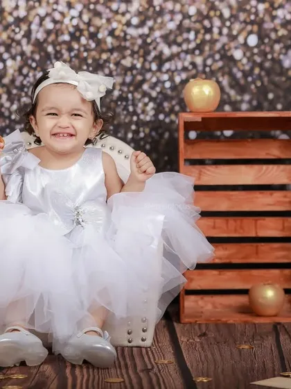 A little princess in a fluffy white dress beams with joy. The glittery background makes her shine even brighter in this happy, celebratory photo.