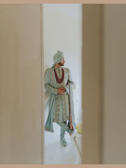 A candid, framed shot of the groom looking out, captured through a doorway. This portrait has a thoughtful and cinematic quality, telling a story without words.