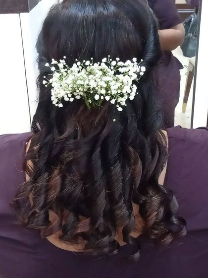 A half-up hairstyle with soft curls, adorned with a sprig of baby's breath. This is a classic and romantic look for any pre-wedding function.
