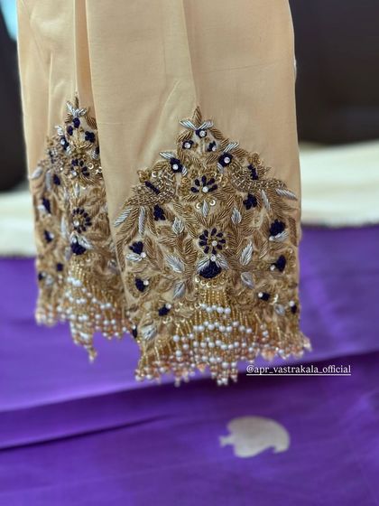 An off-white blouse with heavy zardosi work on the sleeves, in shades of gold and navy.