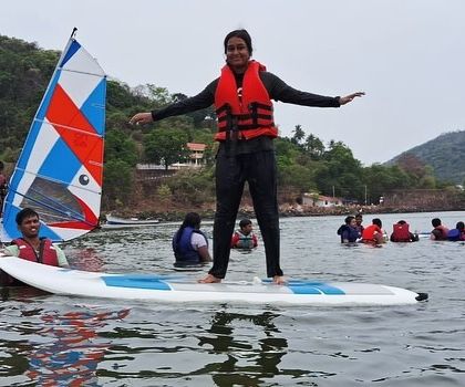 A participant shows off her balance on a paddleboard while a windsurfer sails by in the background at Karwar.