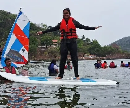A young girl finds her balance on a stand-up paddleboard, surrounded by fellow campers and a windsurfer at our Karwar course.