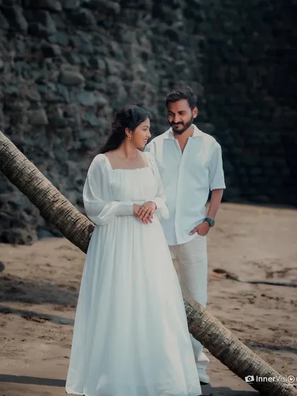 The couple shares a quiet moment, leaning against a fallen palm tree on the beach. This candid interaction captures their gentle connection in a rustic coastal setting.