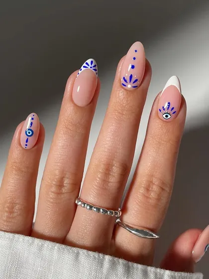A close-up look at our detailed, hand-painted nail art. This set features delicate evil eye and geometric patterns on a natural base, combined with a modern French tip, showcasing our precision and creativity for custom designs.