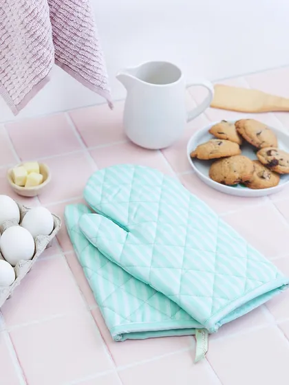 This flat lay composition for Theobroma showcases their baking accessories. The pastel color palette, with mint green oven mitts and pink tiles, creates a fresh and cheerful aesthetic, while the surrounding ingredients hint at the promise of delicious treats.