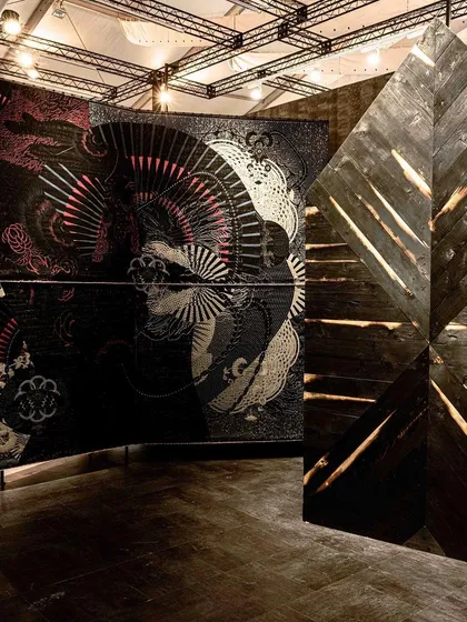 The 'Gothilicious' woven panels stand next to a wall of scarred and burnt wood. This juxtaposition of textures highlights the edgy and vulnerable finishes central to the theme.
