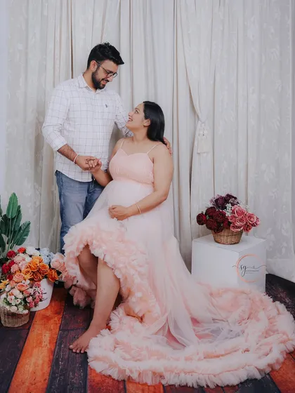 A romantic studio maternity photo with a soft, dreamy feel. The couple shares a loving gaze amidst a setup with flowing drapes and floral accents, creating a truly magical atmosphere.