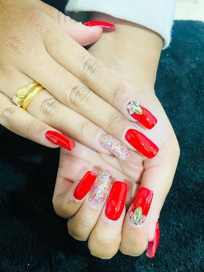 A bold red set on square nails, perfect for a party. The design includes multi-color glitter accent nails and red nails adorned with leaf-shaped rhinestone clusters.