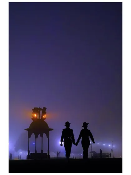 A silhouette of two soldiers holding hands as they walk through the fog during Republic Day rehearsals. The moody, purple twilight and the lantern create a poignant and atmospheric scene.