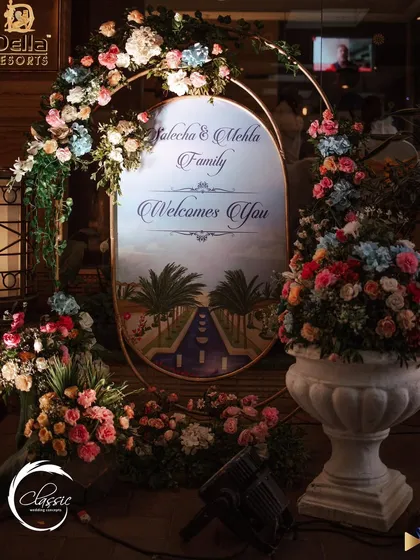This elegant, oval welcome sign is framed by a beautiful arch of pastel-colored roses and hydrangeas, creating a sophisticated and romantic first impression.