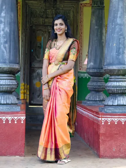 A stunning bridal portrait in a traditional silk saree. The bride is framed by the pillars of a classic South Indian house, creating an elegant and timeless image.
