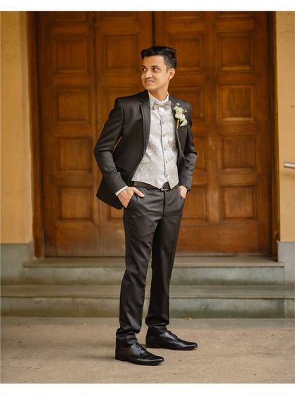 A full-length portrait of the groom looking dapper in his tuxedo. This classic shot showcases his style against a simple, elegant wooden door.