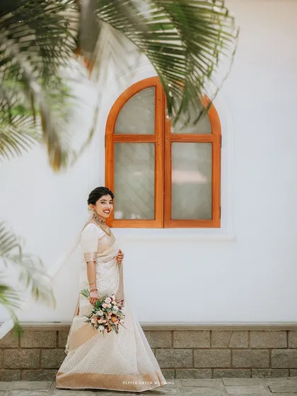 A stylish portrait of the bride framed by a window and a palm frond, blending architecture and nature.