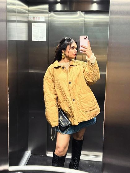 An elevator selfie showing off a casual winter look with an oversized quilted jacket and boots.