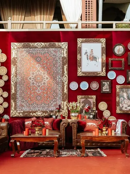 A comfortable and stylish lounge area designed for guests at the 'Laal Ishq' wedding. The setup includes leather sofas, custom cushions, and a backdrop wall that tells a story of Indian heritage and art.