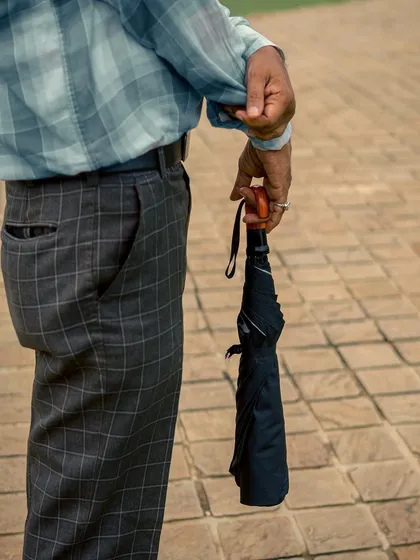 A close-up detail shot of a man's hands holding a closed umbrella. This minimalist image focuses on the textures of the fabric and the simple act of being prepared for the rain.