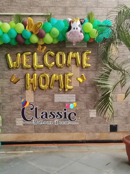 A jungle-themed 'Welcome Home' balloon arch against a brick wall, featuring cute animal foil balloons like a monkey and a lion.