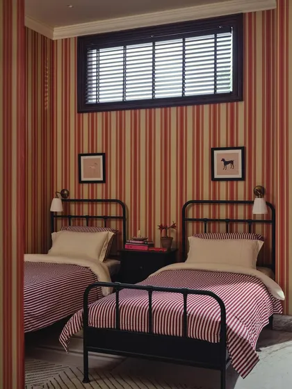 A frontal view of the twin beds in the guest room. The symmetry, high ceilings, and pattern-on-pattern design give this compact room a sense of old-world charm and deliberate composition.