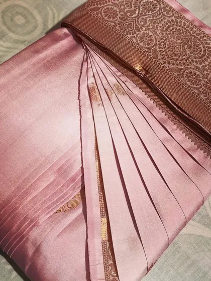 A delicate light pink saree with a bronze border, folded to protect its soft fabric.