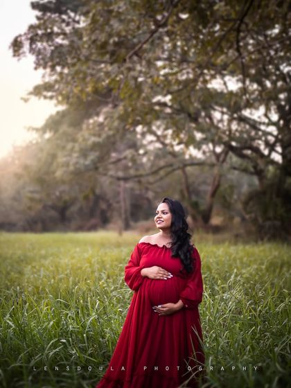 A serene solo portrait in a glowing field at sunset. The deep red dress creates a stunning contrast with the natural surroundings.