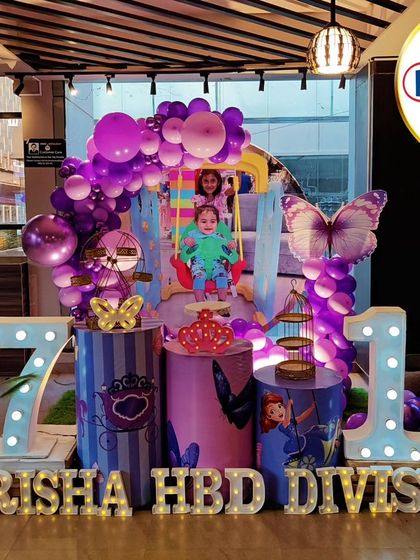 A joint princess-themed birthday for a 7-year-old and 1-year-old. The purple decor features Sofia the First and Ariel cutouts, and light-up numbers '7' and '1'.