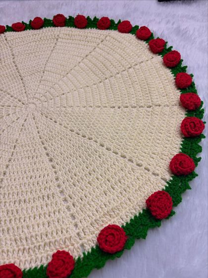 The rose blanket laid flat to show its full 25-inch circular design. The border is adorned with detailed red crochet roses, making it a stunning throw or baby blanket.