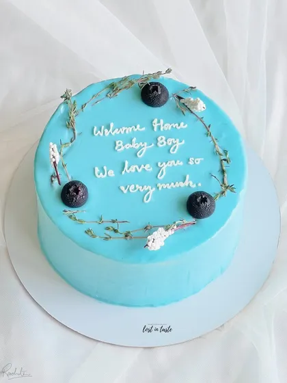 A sweet and simple cake to celebrate a new arrival. This light blue buttercream cake is decorated with delicate herbs and blueberries for a "Welcome Home Baby Boy" party.