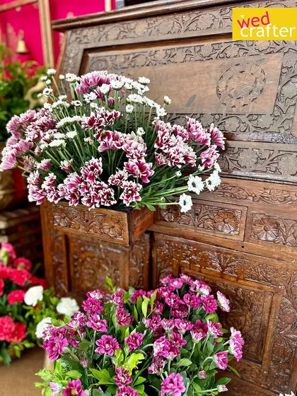 Beautiful purple and white chrysanthemums arranged against a backdrop of an intricately carved antique wooden chest.