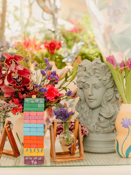 A close-up of a table setting with a mix of modern and classic elements, including a Greek-style bust, colorful Jenga blocks, and fresh flowers.