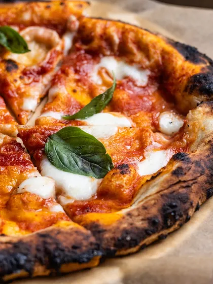 A close-up of our classic Margherita pizza, showing the beautiful char on the crust and the fresh basil leaves. It's a simple crime not to share.