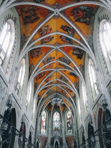 An upward-looking shot of the stunning, painted vaulted ceiling of a church. The intricate details and symmetrical arches create a sense of awe and reverence, showcasing the city's hidden architectural gems.