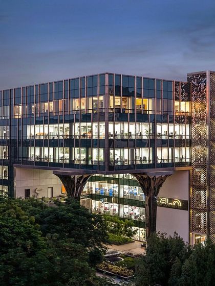 A wide shot of the Stainless Steel Office building at dusk. The image captures the glowing interiors, the shimmering steel facade screen, and the iconic faceted columns, showcasing the full impact of our design interventions.
