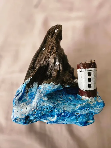 Another angle of a driftwood piece in progress. The focus here is on creating the texture of the churning sea against the rugged cliff and the solitary lighthouse. It’s a study in how paint and natural wood can create a dramatic, moody scene.