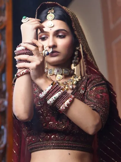 A candid moment of the bride adjusting her bangles. The makeup remains flawless, with a focus on glowing skin and defined, expressive eyes.