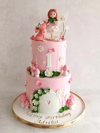 A sweet fairy-themed cake for Advika's first birthday. The two-tiered pink cake features a fairy house, mushrooms, and a cute little dragon.