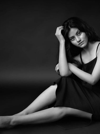 A seated black and white portrait with a moody, contemplative feel. The lighting creates soft shadows, adding depth and emotion to the image.