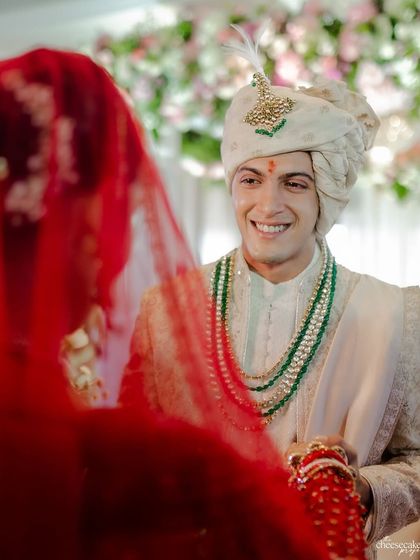 The groom's smile as he sees his bride for the first time, framed by her red veil. A classic, timeless wedding photograph.