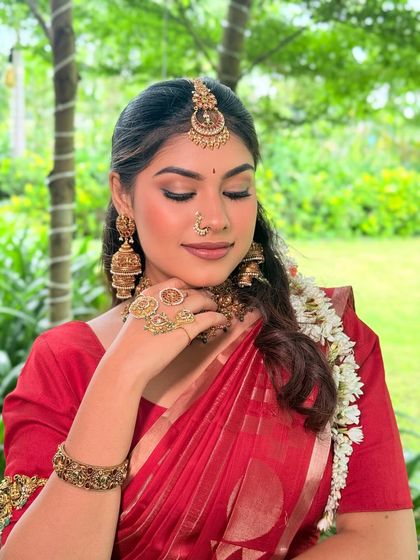 The soft, shimmery eye makeup and neutral lip perfectly complement the warm tones of the antique gold jewellery and the vibrant red saree.