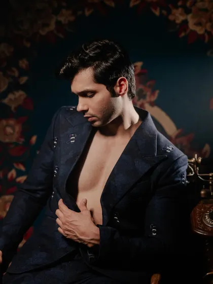 Abhishek Kumar in a navy blue patterned suit. The jacket is worn open to create a relaxed yet sophisticated look, with subtle metallic embellishments on the shoulders and lapels adding a touch of evening glamour.