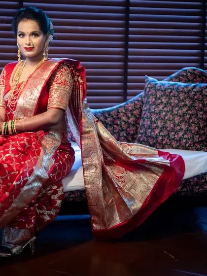 A poised bridal portrait, with the bride seated elegantly in her rich red wedding saree.